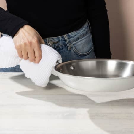 hand grabbing hot stainless-steel skillet with Now Designs Ripple Kitchen Towel.